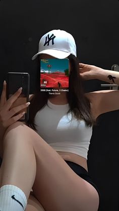 a woman in white shirt and black shorts holding a cell phone with her legs crossed