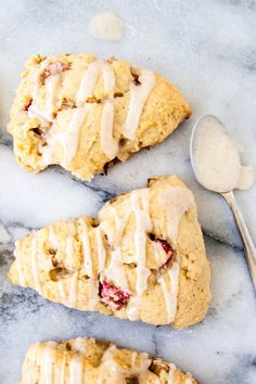 three scones with icing sitting on top of a marble counter next to a spoon