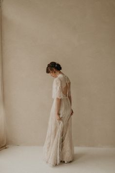 a woman standing in front of a window wearing a white dress with sheer sleeves and an open back