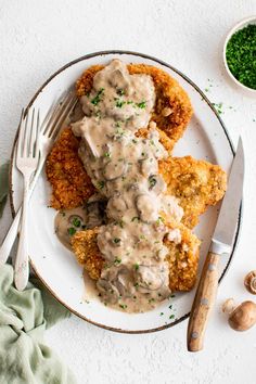 a white plate topped with fried chicken covered in gravy next to a knife and fork