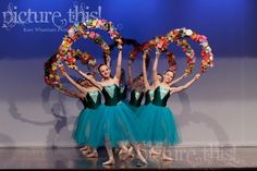 four ballerinas in green tutu skirts holding wreaths on their heads and arms