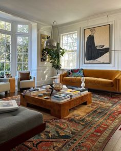 a living room filled with lots of furniture next to two large windows and a painting on the wall