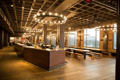 an empty restaurant with wooden tables and benches in the center, lights hanging from the ceiling