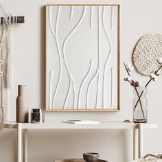 a white table with a vase and some flowers on it next to a framed art piece