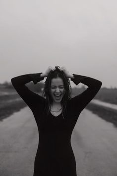 a woman standing on the side of a road holding her hair in front of her head