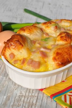 an egg and ham casserole in a white dish on a wooden table next to eggs