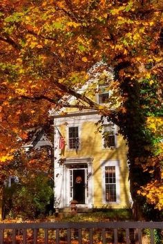 a yellow house surrounded by trees with fall foliage