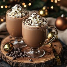 two glasses of hot chocolate drink with whipped cream and chocolate chips on a wooden board