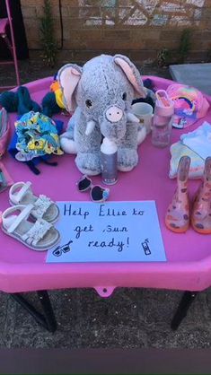 a pink table topped with stuffed animals and other items on it's side, next to a sign that says help eliie to get sun ready