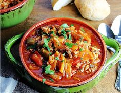 two bowls filled with chili and beans on top of a wooden table next to bread