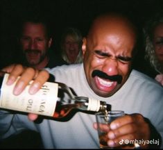 a man with a moustache on his face holding a bottle of alcohol in front of people