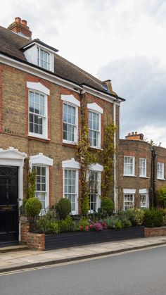 a large brick building with many windows and plants in the middle of the street next to it