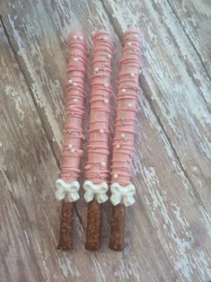 three pretzels with pink icing and bows on them sitting on a wooden table