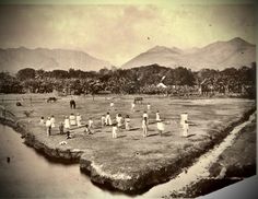 an old black and white photo of people playing baseball in a field with mountains in the background