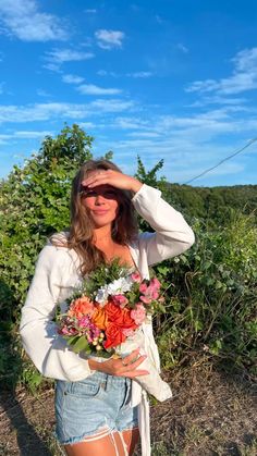 a woman holding a bouquet of flowers in front of her face while standing on a field