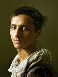 a young man with short hair is posing for a photo in front of a dark background