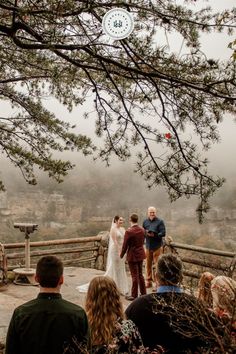 a bride and groom are getting married on the top of a hill with fog in the background