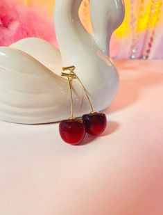 two cherries are attached to a white swan figurine on a pink surface