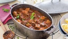 a large pot filled with stew next to pasta and other food on a table top