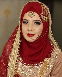 a woman wearing a red hijab with gold jewelry and makeup on her face