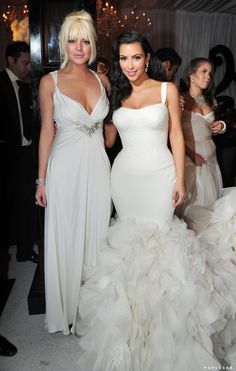 two women in white dresses standing next to each other at a formal event, posing for the camera