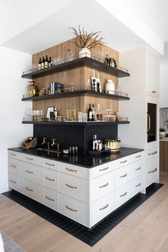 a kitchen with white cabinets and black counter tops, gold trim on the shelves is filled with wine bottles