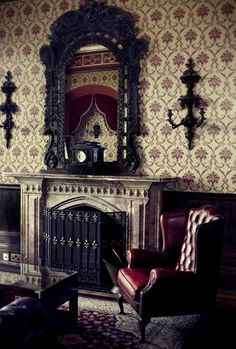 a living room with a fireplace and ornate wallpaper on the walls, along with a red chair