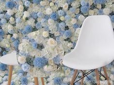 two white chairs are facing each other in front of a wall with blue and white flowers