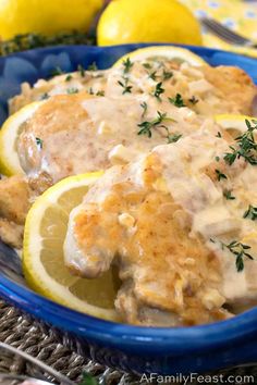 a blue bowl filled with chicken and gravy next to lemons