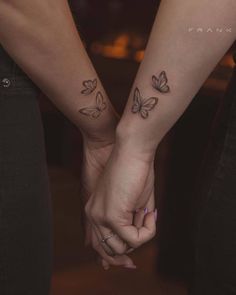 two people holding hands with butterfly tattoos on their wrist and the other hand behind them