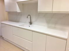 a kitchen with white cabinets and marble counter tops, including a stainless steel faucet