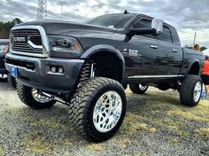 a large black truck parked on top of a gravel lot next to other trucks and people