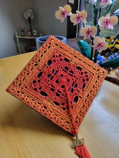 an orange crocheted square with a tassel hanging from it's end