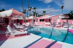 a pool with chairs and umbrellas next to a pink house that has palm trees in the background