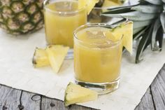 two glasses filled with pineapple punch sitting on top of a table next to sliced pineapples