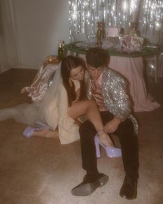 a man and woman sitting on the floor in front of a table with lights behind them