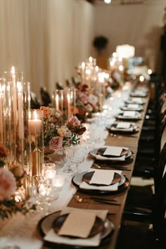 a long table is set with black and white plates, silverware, candles and flowers