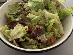 a bowl filled with lettuce and tomatoes on top of a table