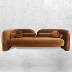 a brown couch with pillows on it sitting in front of a white wall and concrete floor