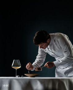 a man in chef's uniform preparing food on a table with a glass of wine