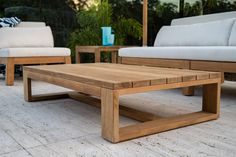 a wooden coffee table sitting on top of a white tile floor next to two couches