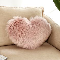 a pink heart shaped pillow sitting on top of a beige couch next to a plant