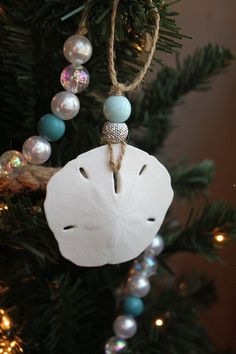 a white sand dollar ornament hanging from a christmas tree with beads and lights