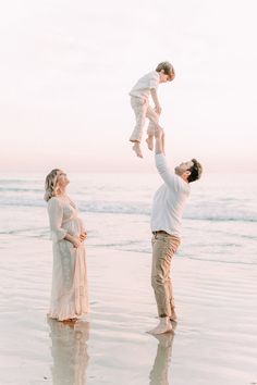 a man and woman holding up a baby on the beach