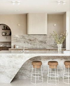 three stools sit in front of an island with marble countertops and shelves on the wall