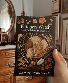 a person holding up a book about kitchen witch