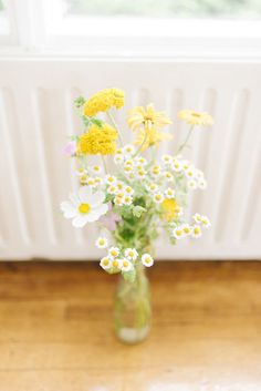 a vase filled with yellow and white flowers on top of a wooden floor next to a radiator