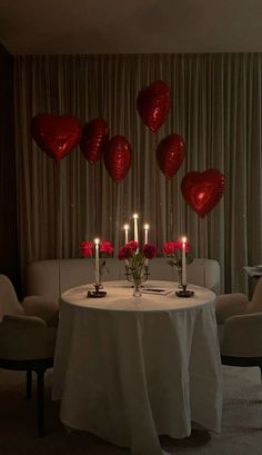 a table with candles and red heart balloons on it in front of a curtained window