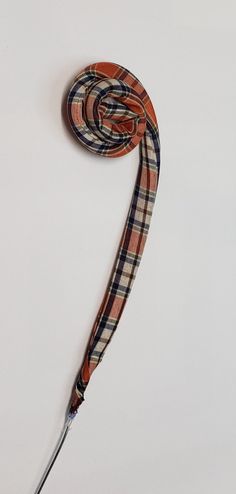 an orange and black plaid leash with a metal hook on it's end, hanging from a white wall