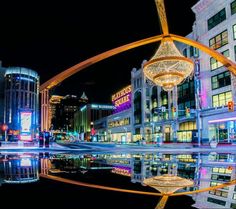 a city street filled with lots of tall buildings next to a river and lit up at night